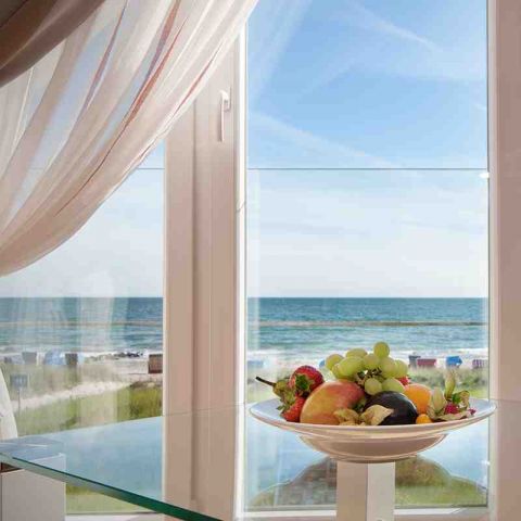 Zimmer Hotel Haus am Meer, Blick durch Fenster auf blaue Ostsee, vor dem Fenster Glastisch mit Obstteller