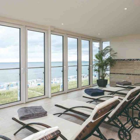 Hotel Haus am Meer, Wellnessbereich, Wellnessliegen in einer Reihe mit Blick durch die Fensterfront auf die Ostsee, rechts in der Ecke große grüne Topfpflanze, auf den Liegen Handtücher