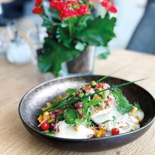 Restaurant Hotel Haus am Meer, Tisch mit Blume und Salz- und Pfefferstreuer, im Vordergrund schwarzer Teller mit Fischgericht