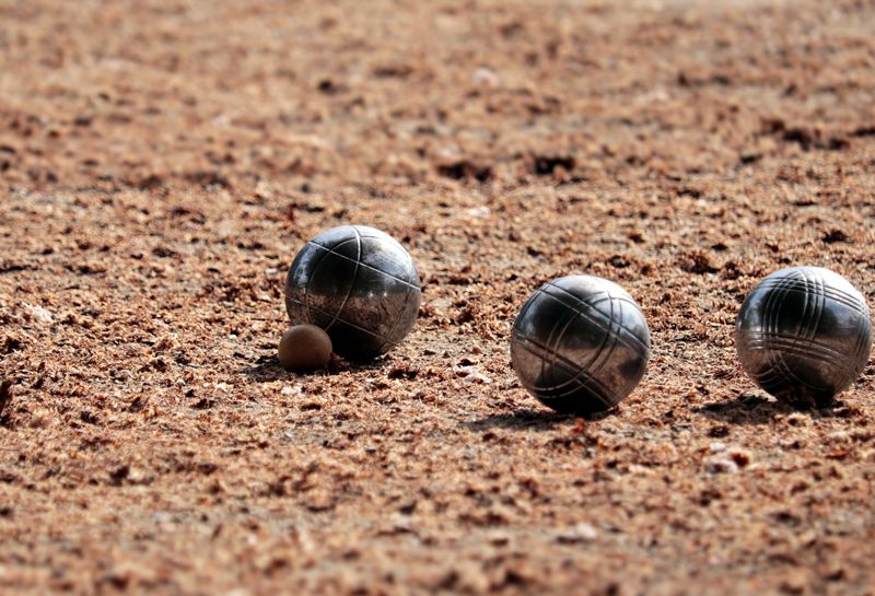 Aktivitäten Howachter Bucht, Boule, Nahaufnahme von drei großen und einer kleinen Metallkugel, Kugeln liegen auf dem Sandboden