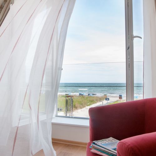 Blick auf die Ostsee. Die großen Fenster stehen auf und vor ihnen stehen zwei rote Sessel