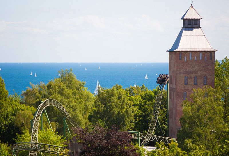 Aktivitäten Howachter Bucht, Attraktion Flucht von Novgorod im Hansa Park, Attraktion inmitten von grünen Bäumen, im Hintergrund Blick auf Ostsee mit vielen Segelschiffen