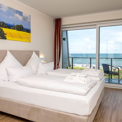Appartement Schlafzimmer mit Fensterfront. Gemachtes Doppelbett und Ausblick auf die Ostsee. Tür führt zum Balkon