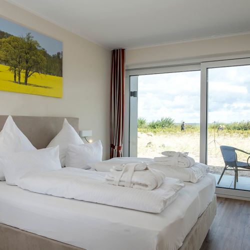 Appartement Schlafzimmer mit Fensterfront. Gemachtes Doppelbett und Ausblick auf die Ostsee
