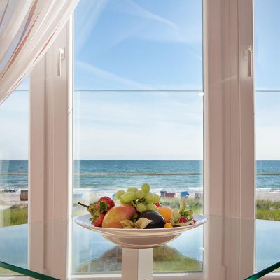 Zimmer Hotel Haus am Meer, Blick durch Fenster auf blaue Ostsee, vor dem Fenster Glastisch mit Obstteller