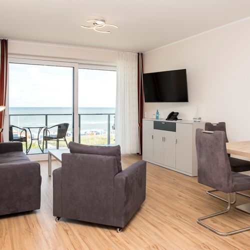 Exclusive Appartement Wohnzimmer mit grauer Couch und grauen Stühlen. Ausblick auf die Ostsee aus der bodentiefen Fensterfront vom Wohnzimmer