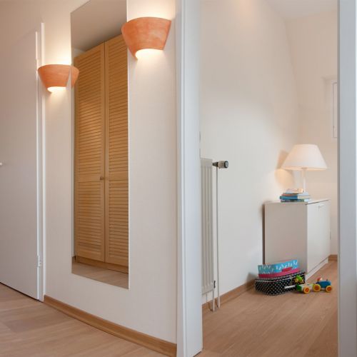 Flur mit einem Spiegel und zwei Lampen. Man sieht in einen anderen Raum in dem Kinder Spielzeug liegt