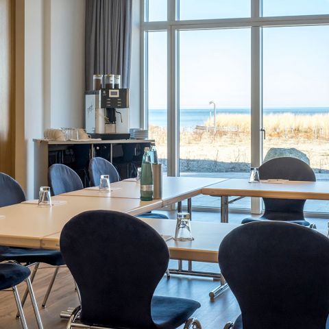 Tagen Hotel Haus am Meer, Tagungsraum, Bestuhlung U-Form, Tische gedeckt mit Wassergläsern, Wasserflaschen, Blöcken, in der linken Ecke Rollwagen mit Kaffeevollautomat und Tassen, Blick auf die Ostsee