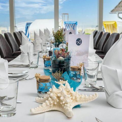Feierlichkeiten Haus am Meer, festlich geschmückte Tafel in der Lobby am Fenster, Teller, Besteck, Gläser, gefaltete Servietten, maritime Deko mit Seesternen, Muscheln, Blick auf die Sonnenterrasse