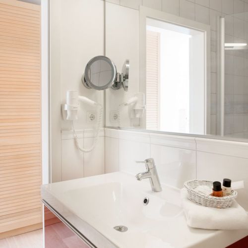 Badezimmer des Doppelzimmer in weiß mit roten Unterschränken. Frische Handtücher und ein kleiner Korb mit Seife stehen auf dem Waschbecken