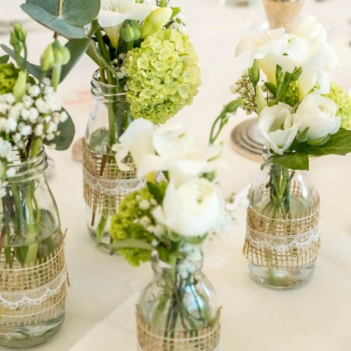 Feierlichkeiten Haus am Meer, Nahaufnahme kleine Glasvasen mit Blumensträußen in weiß/grün gehalten