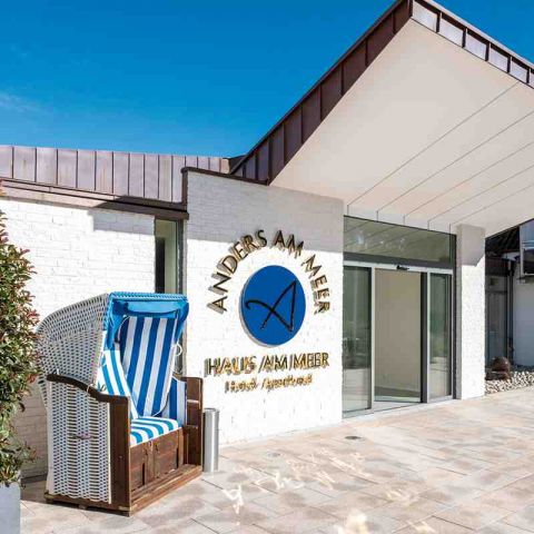 Hotel Haus am Meer, Haupteingang, links Strandkorb, daneben an der Hauswand großes Logo Haus am Meer, daneben Eingang mit automatischen Türen, Überdachung beim Eingang