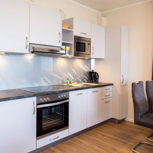 Exclusive Appartement Küche in modernen weiß und grau Tönen. Herd, Kochplatte und Mikrowelle sind vorhanden.