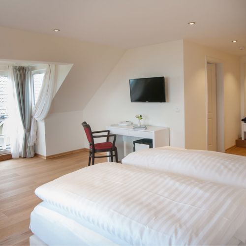 Doppelzimmer mit Blick in den Raum rein. Ein kleiner Schminktisch mit Stuhl und Blumen