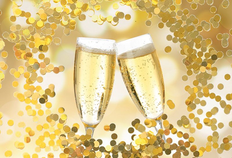 Arrangements Haus am Meer, Silvester, Hintergrund verschwommene Lichtflecken, zwei anstoßende Sektgläser, um die Gläser herum goldenen Pailletten