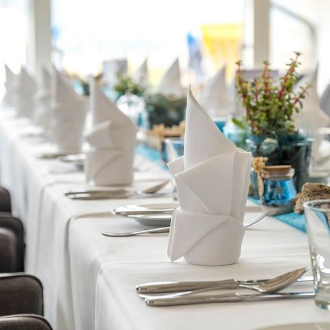 Feierlichkeiten Haus am Meer, festlich geschmückte Tafel in der Lobby am Fenster, Teller, Besteck, Gläser, gefaltete Servietten, maritime Deko, Blick auf die Sonnenterrasse
